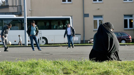 Auf einem Platz spielen Männer Fußball, davor sitzt eine Frau mit Kopftuch. © dpa - Bildfunk Foto: Holger Hollemann