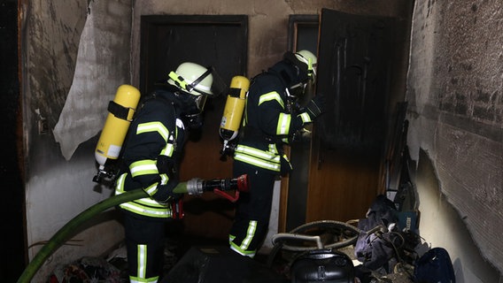 Zwei Einsatzkräfte der Feuerwehr löschen einen Brand durch eine Wohnungstür. © Kreisfeuerwehr Lüchow-Dannenberg 