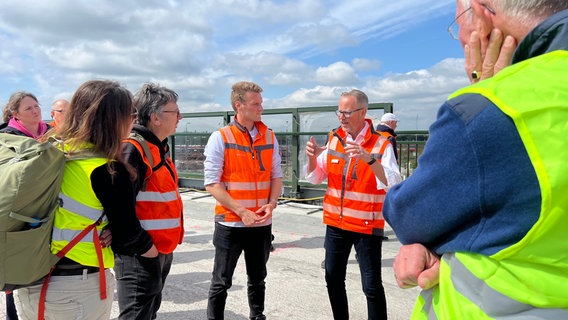 Der Bauleiter und der Projektleiter stehen mit Warnweste auf der Decatur-Brücke und informieren eine Gruppe. © NDR Foto: Marlene Kukral
