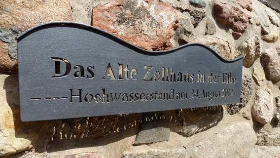 Ein schwarzes Metallschild hängt an einer Steinwand. Darauf steht "Das Alte Zollhaus in der Elbe". © NDR Foto: Alina Stiegler