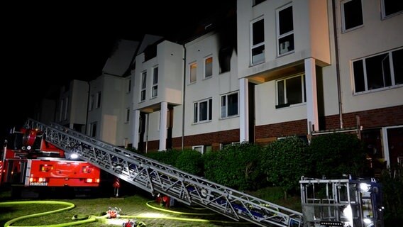 Nach einer Explosion in einem Wohnhaus in Lüneburg sind Rußflecken an einem Fenster zu sehen, Feuerwehrleute sind am Einsatzort. © NEWS5 