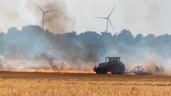 Ein Traktor fährt an einem Feldbrand vorbei. © Joto/JOTO/dpa 