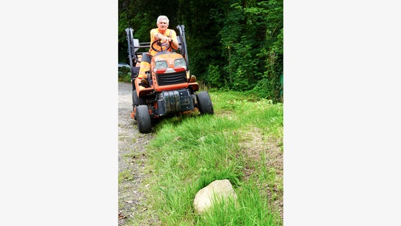 Ein Mitarbeiter des Betriebshof sitzt auf einem Rasenmäher und zeigt auf einen Findling auf dem Grünstreifen. © Gemeinde Seevetal 