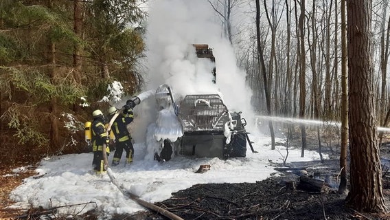 Feuerwehrleute löschen mit Schaum eine im Wald stehende brennende Forstmaschine. © Kreisfeuerwehr Lüchow-Dannenberg 