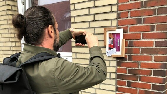 Der Künstler mit Namen "Framespotting" macht ein Foto von einem Bild an einer Hauswand auf. © NDR Foto: Christoph Deuschle