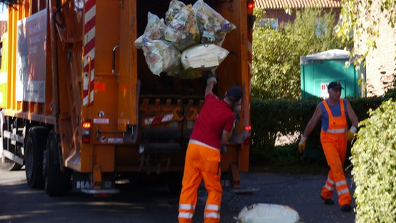 Ein Mitarbeiter der Müllabfuhr wirft gelber Säcke in einen orange-farbenen Müllwagen. © NDR Foto: Dirk Drazewski