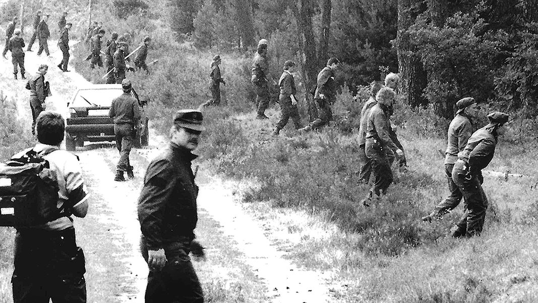 Auf einem alten schwarzweiß-Foto sind Dutzende Polizisten zu sehen, die ein Waldstück durchkämmen.