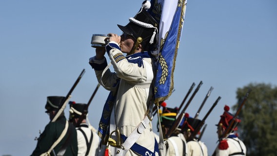 Ein als Soldat verkleideter Laienschauspieler trinkt aus einer Feldflasche. Im Hintergrund sind weitere Soldaten in historischen Kostümen zu sehen, die die sogenannte Göhrdeschlacht vom 16. September 1813 nachstellen. © Björn Vogt/dpa Foto: Björn Vogt