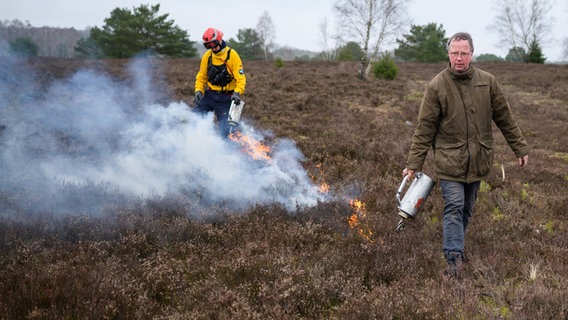 Dirk Mertens (r), Stiftung Naturschutzpark Lüneburger Heide, und ein Feuerwehrmann setzen mit einer Flämmkanne eine Heidefläche in Brand. © dpa Foto: Philipp Schulze