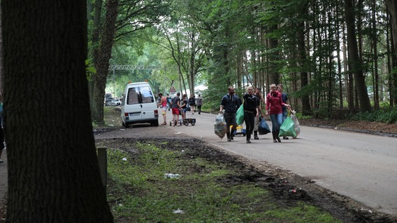 Festivalbesucher tragen Müllsäcke über eine Straße. © NDR Foto: Adrian Lange