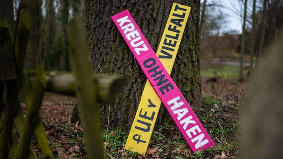 Ein Holzkreuz mit der Aufschrift Kreuz ohne Haken - für Vielfalt lehnt an einem Baum. © dpa Foto: Philipp Schulze