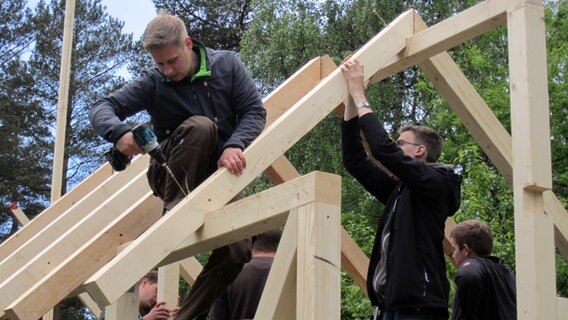 Eine Gruppe junger Männer befestigen Holzbalken für ein Dach einer Hütte.  