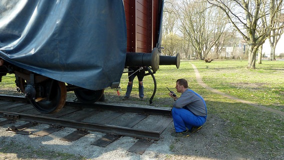 Ein Mann funkt über ein Funkgerät, während ein Güterwaggon auf die Gleise herabgelassen wird. © NDR Foto: Karin Hansen