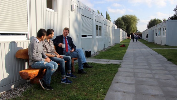 Mohammad und Abdullahh Abd und Christian Berndt sitzen auf einer Bank in einer Containerwohnanlage. © NDR Foto: Andreas Rabe