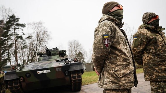 Ukrainische Soldaten stehen auf dem Truppenübungsplatz in Munster vor reinem Panzer. © dpa Foto: Christian Charisius