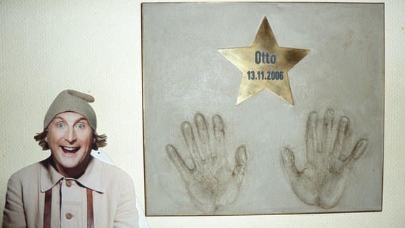 Otto Waalkes steht neben einer Ehrentafel anlässlich des Films "7-Zwerge" © NDR 