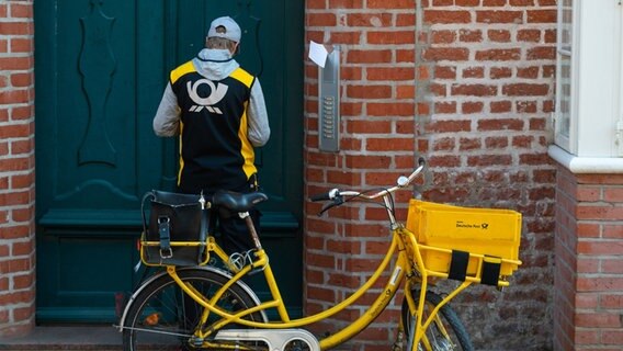 Ein Postbote steht mit seinem Fahrrad vor einer Haustür. © picture alliance/dpa/Philipp Schulze Foto: Philipp Schulze