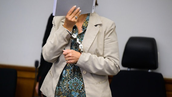 Lüneburg: Eine Angeklagte steht mit Handschellen im Saal vom Landgericht und verdeckt ihr Gesicht. © picture alliance/dpa Foto: Philipp Schulze