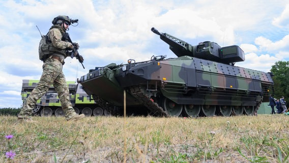 Ein "Infanterist der Zukunft" steht neben einem Schützenpanzer Puma des Rüstungskonzerns Rheinmetall bei einer Führung durch das Rheinmetall-Werk Unterlüß. © picture alliance/dpa/Julian Stratenschulte Foto: Julian Stratenschulte