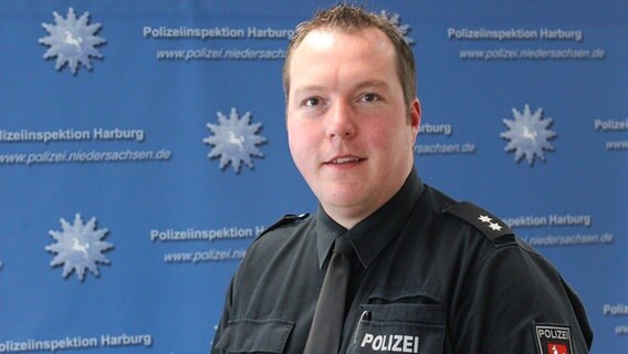 Jan Krüger steht vor einer Werbewand der Polizeiinspektion Harburg. © NDR Foto: Ann-Krisitn Mennen