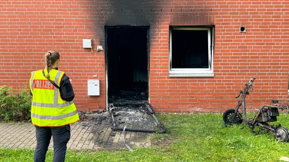 Eine Polizistin steht neben einem verbrannten E-Scooter und einem Brandschaden an einem Studentenwohnheim in Lüneburg. © JOTO 