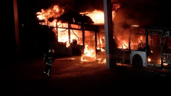 Ein Feuerwehrmann löscht einen brennenden Bus auf einem Firmengelände in Sittensen im Landkreis Rotenburg. © Hellwig TV Elbnews Produktion 