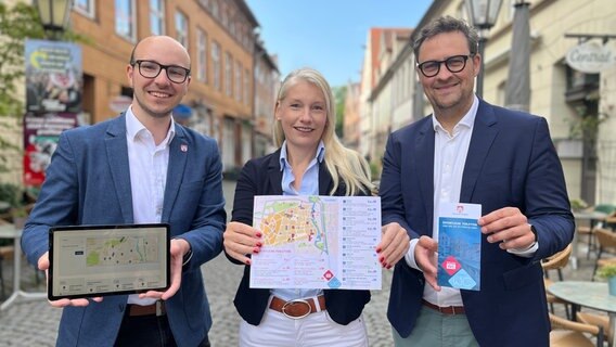 Finn Kubisch, Sonja Jamme und Carl-Ernst Müller halten Stadtpläne und Flyer zum StadtWC in der Hand. © Hansestadt Lüneburg 