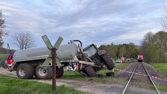 Ein Traktor steht mit einem Anhänger nach einem Zusammenstoß mit einem Zug an einem Bahnübergang. © Polizeiinspektion Rotenburg 