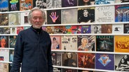 Der Künstler Klaus Voormann steht vor LP-Covern in einer Ausstellung. © NDR Foto: Marlene Kukral