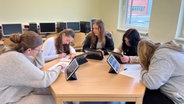 Schülerinnen sitzen um einen Tisch mit iPads in den Händen in einem Klassenraum der KSG Bad Bevensen in der Hand. © NDR Foto: Marlene Kukral