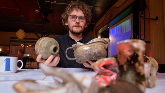 Der Archäologe Attila Dezsi hält einen Atemschutzmaskenfilter und einen Topf in den Händen. © dpa-Bildfunk Foto: Philipp Schulze