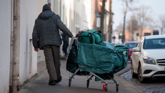 Ein vermutlich wohnungsloser Mann zieht einen Einkaufswagen mit Rucksack und Tasche hinter sich her. © dpa Bildfunk Foto: Philipp Schulze
