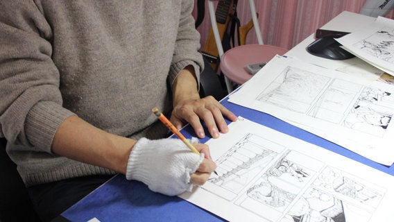 Eine Person zeichnet ein Manga-Comic an einem Tisch. © picture alliance / Kyodo Foto: Kyodo