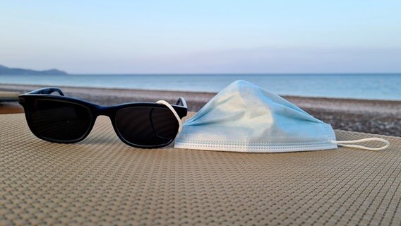 Eine Maske und eine Sonnenbrille liegen auf einer Liege am Strand. © picture alliance / Kirchner-Media | Marco Steinbrenner/Kirchner-Media Foto: Marco Steinbrenner