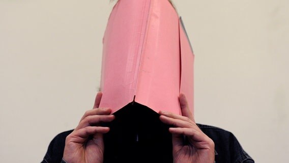Der als "Maskenmann" bekannt gewordene Martin N. bedeckt sein Gesicht in einem Gerichtssaal mit einem Aktenordner. © picture alliance/dpa/David Hecker Pool Foto: David Hecker Pool