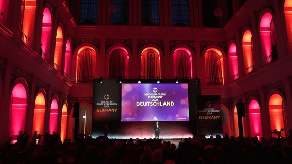 Die Bühne bei Verleihung der Michelin-Sterne 2024 leuchtet rot. © dpa-picture alliance Foto: Marcus Brandt