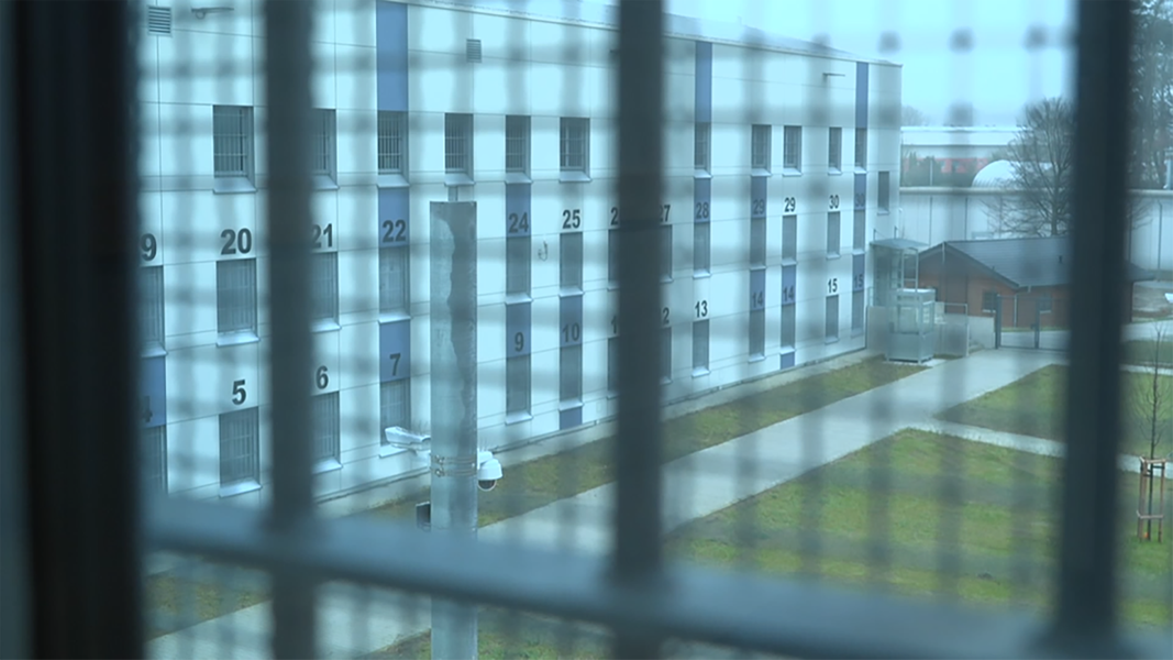 Durch ein Gitterfenster sieht man den Innenhof von einem Gefängnis.