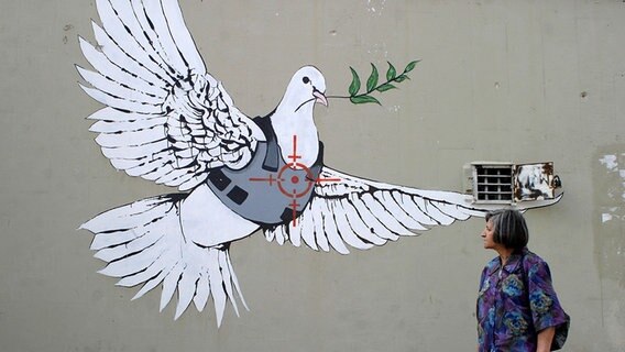 Eine Touristin betrachtet eine Friedenstaube, welche auf eine Wand gesprüht ist. © picture alliance/ landov Foto: Najeh Hashlamoun