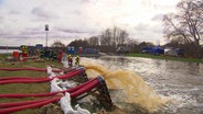 Wasser wird durch große rote Schläuche abgepumpt. Im Hintergrund stehen THW-Fahrzeuge. © NDR 