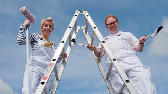 Britta von Lucke und Lars Cohrs stehen im Maleroutfit auf einer Leiter. © NDR Foto: Erwin Neu