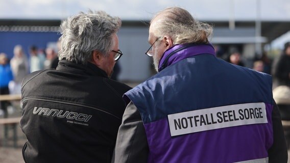 Zwei Männer unterhalten sich, einer trägt eine lilafarbende Jacke mit der Aufschrift "Notfallseelsorge". © dpa - picture alliance Foto: Matthias Bein