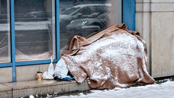 Ein Obdachloser liegt mit Schnee bedeckt vor einem Schaufenster. © picture alliance / imageBROKER | Raimund Kutter Foto: Raimund Kutter