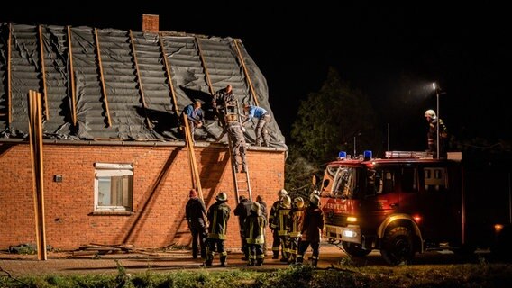 Helfer und Feuerwehrleute decken das Dach eines vom Sturm zerstörten Gebäudes ab. © dpa-Bildfunk Foto: Mohssen Assanimoghaddam