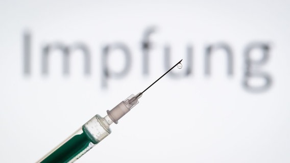 A drop hangs from the tip of a needle. Behind the word "vaccination". © picture alliance / Friso Gentsch / dpa Photo: Friso Gentsch