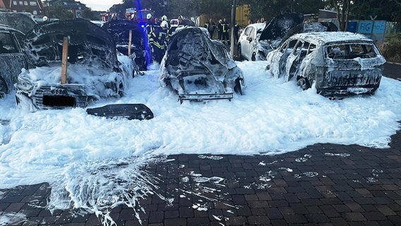 Pkw stehen bedeckt mit Löschschaum auf einem Parkplatz nach einem Brand. © Feuerwehr Landkreis Leer 