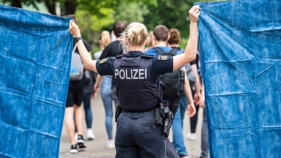 Eine Polizistin schirmt mit Hilfe von Planen Schülerinnen und Schüler ab, die aus der Schule geführt werden. © picture alliance/dpa/Sina Schuldt Foto: Sina Schuldt