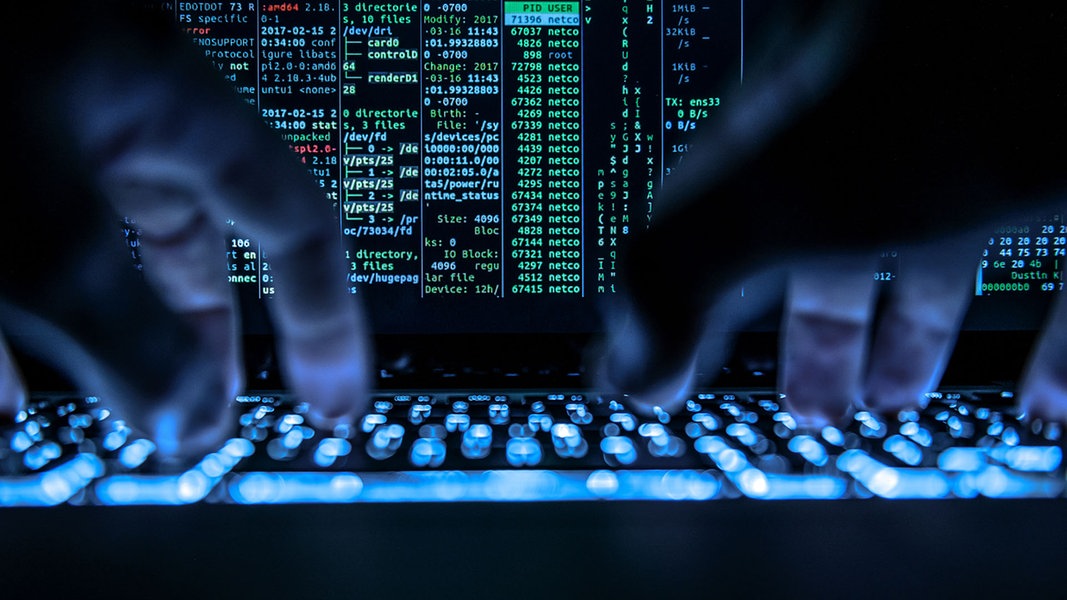 Ein Mann tippt auf der beleuchteten Tastatur eines Laptops, auf dem Bildschirm ist ein Hackerprogramm geöffnet. 