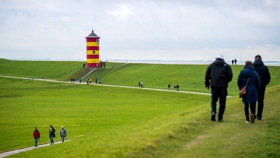 Spaziergänger laufen über den Deich vor dem Pilsumer Leuchtturm. © picture alliance Foto: picture alliance/dpa | Sina Schuldt