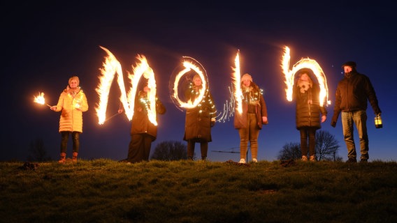 Mehrere Personen schreiben während einer Langzeitbelichtung das Wort "Moin" mit Feuer in die Luft. © Wangerland Touristik 