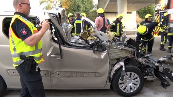 Polizei und Feuerwehr stehen neben einem im Frontbereich stark zerstörten Auto, das nach einem Unfall auf der Autobahn steht. © Nord-West-Media TV 